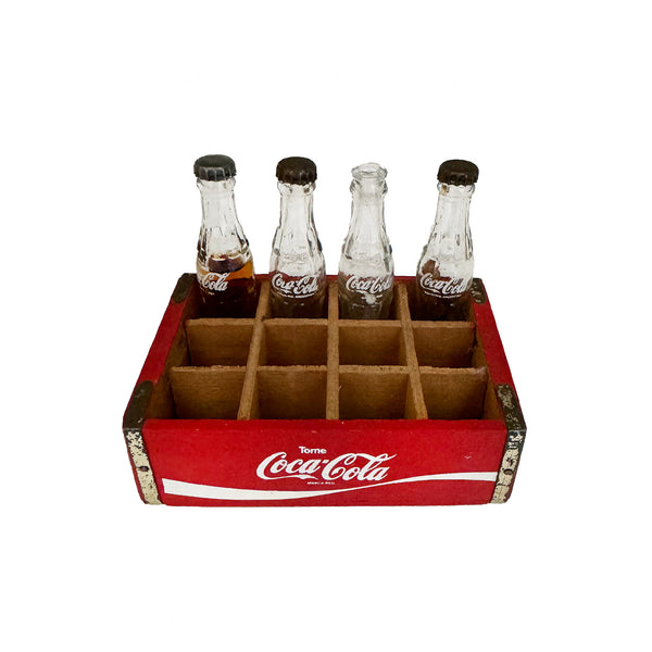 A vintage miniature Coca Cola crate with four bottles, divided into a red wooden box.