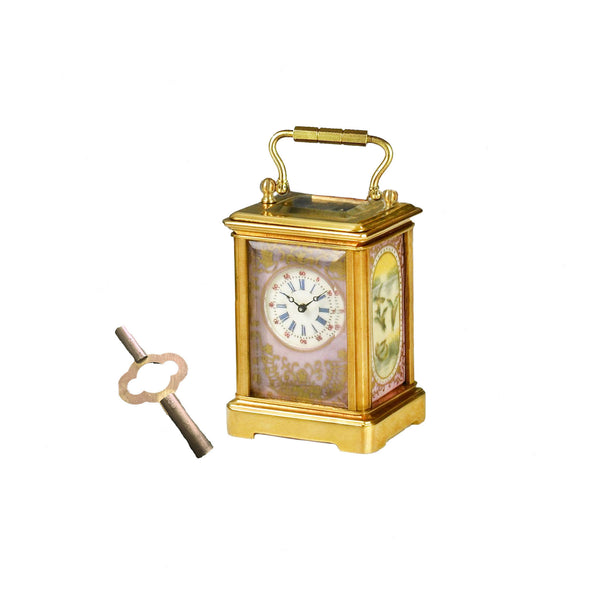 miniature brass carriage clock with pink porcelain panels and key on white background