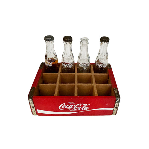 A vintage miniature Coca Cola crate with four bottles, divided into a red wooden box.