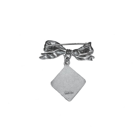 Silver bow-shaped brooch with a diamond-shaped pendant on a white background