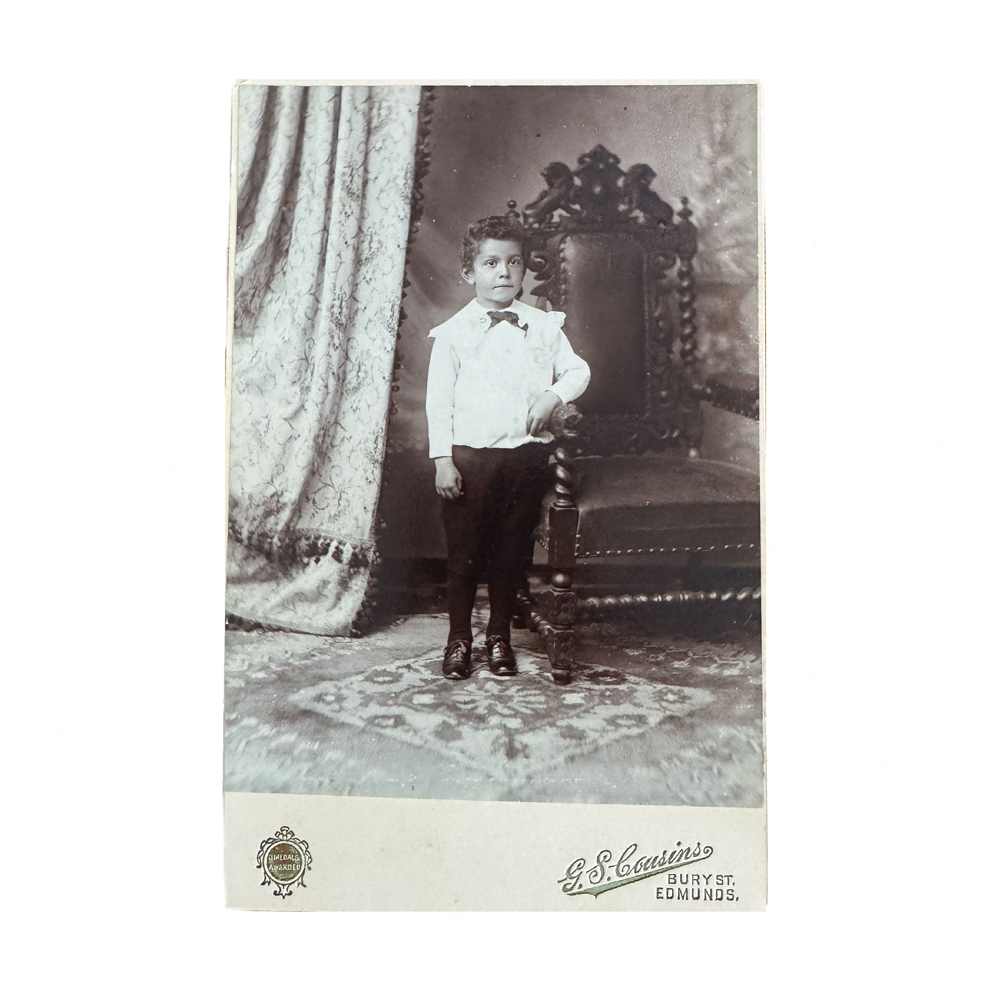 antique black and white photo of a young boy in formal attire sitting on an ornate chair.