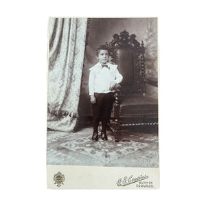 antique black and white photo of a young boy in formal attire sitting on an ornate chair.