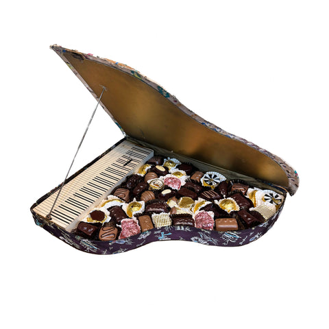 Piano-shaped box filled with assorted chocolates on a white background