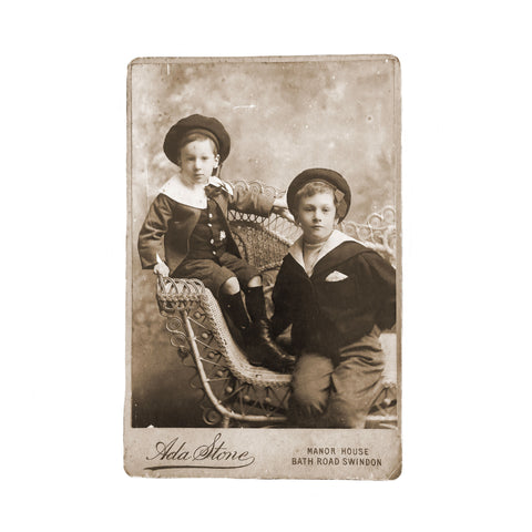Vintage photograph of two boys in formal attire sitting on a decorative bench.