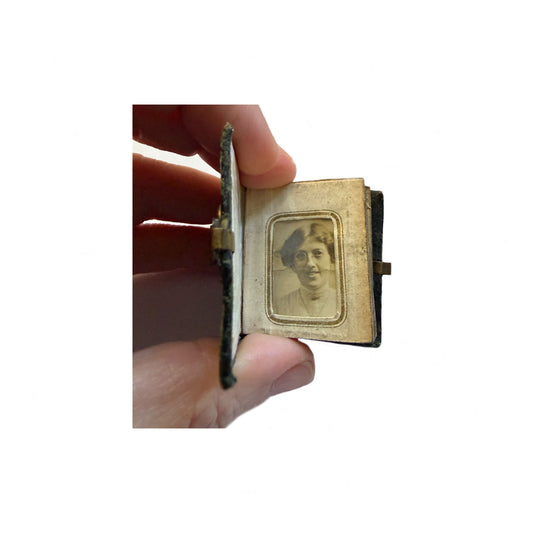 Small antique photo album held by a hand with a portrait inside.