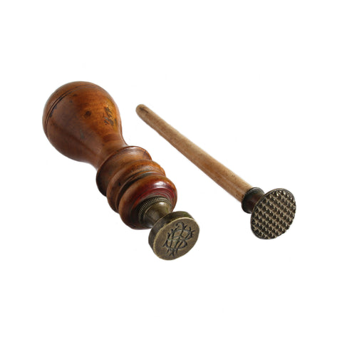 An image of two antique sealing wax seal stamps with brass bases. One stamp has a cross-hatch pattern and the other has initials etched on it.